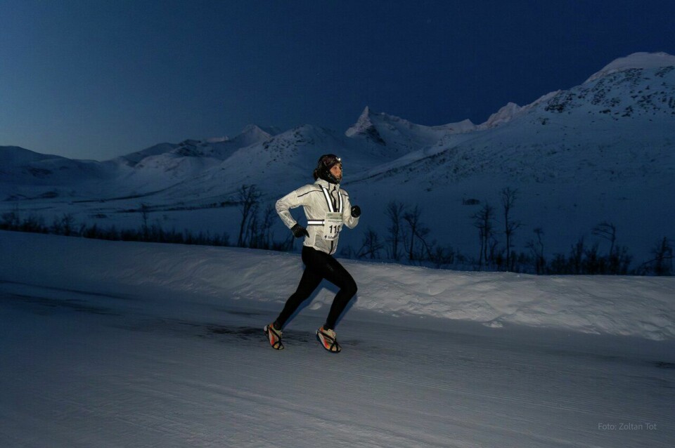 Yngvild Kaspersen i front, med brodder på beina i den snødekte løypen. Og rundt henne polarnatten. (Foto.: Polar Night Marathon/Zoltan Tot) Polar Night Marathon 2025