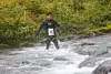 Deltaker med startnummer 23 står i en stri elv omgitt av skog og steiner.