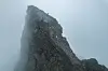 Skarp, mørk fjellkam som stiger opp gjennom tett tåke.