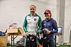 En mann og en kvinne i løpeklær står foran en bygning med medaljer og løpeutstyr.